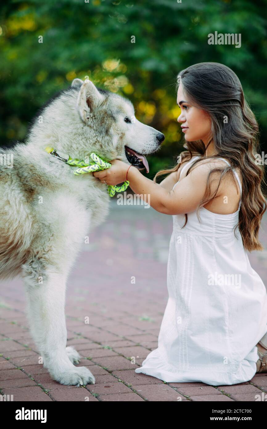 Young woman with innate disorder dwarfism embraces Malamute dog while walking in park. Stock Photo