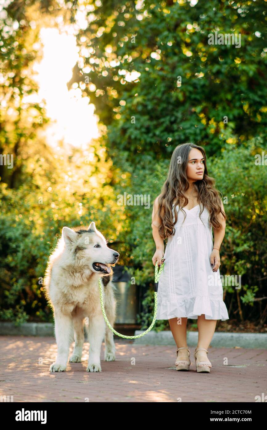 Young woman with innate disorder dwarfism leads on a leash Malamute dog while walking in park. Stock Photo