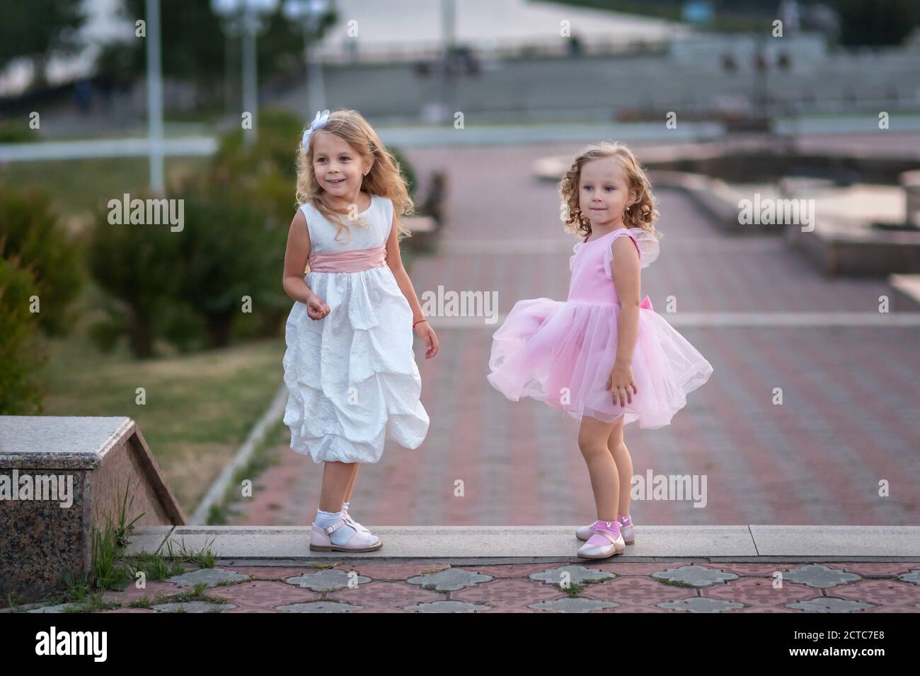 Two little girls in pink and white dressses walking on the street Stock ...