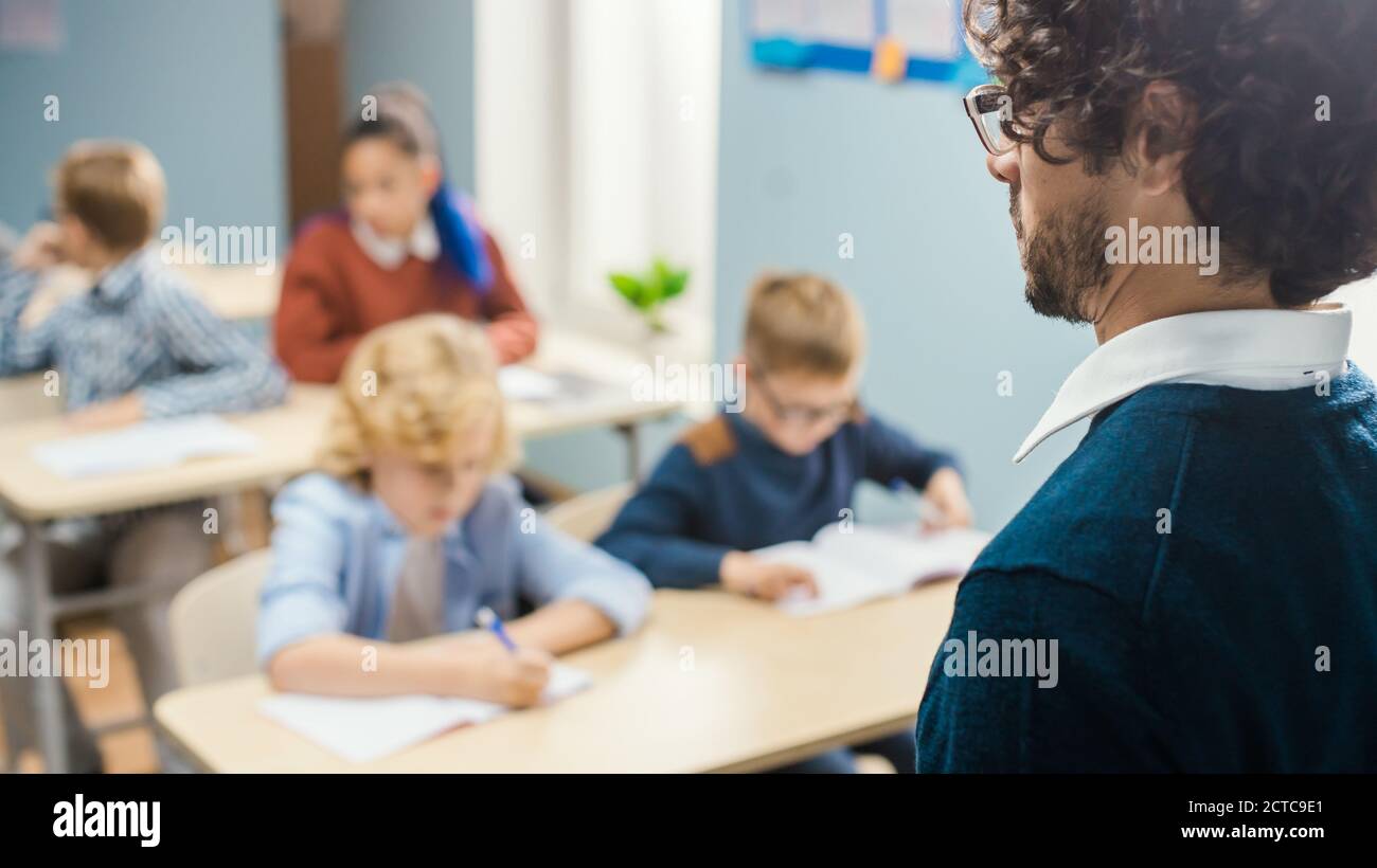 Over the Soulder Shot of Teacher Explaining Lesson to Classroom Full of Diverse Bright Children, In Elementary School Group of Smart Multiethnic Kids Stock Photo