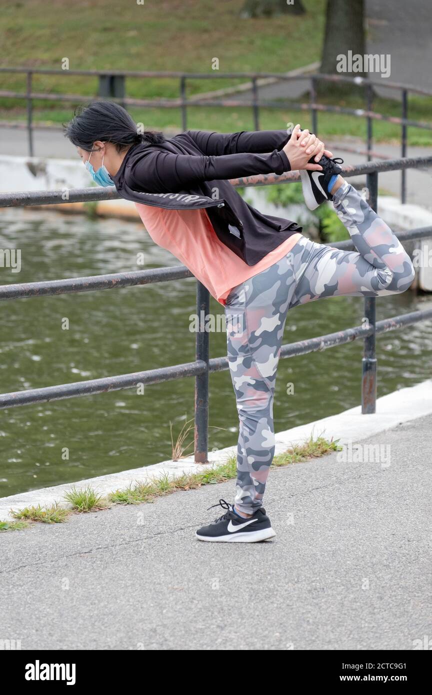 A very limber & nimble Asian American woman stretches before exercising. In a park in Flushing, New York City. Stock Photo