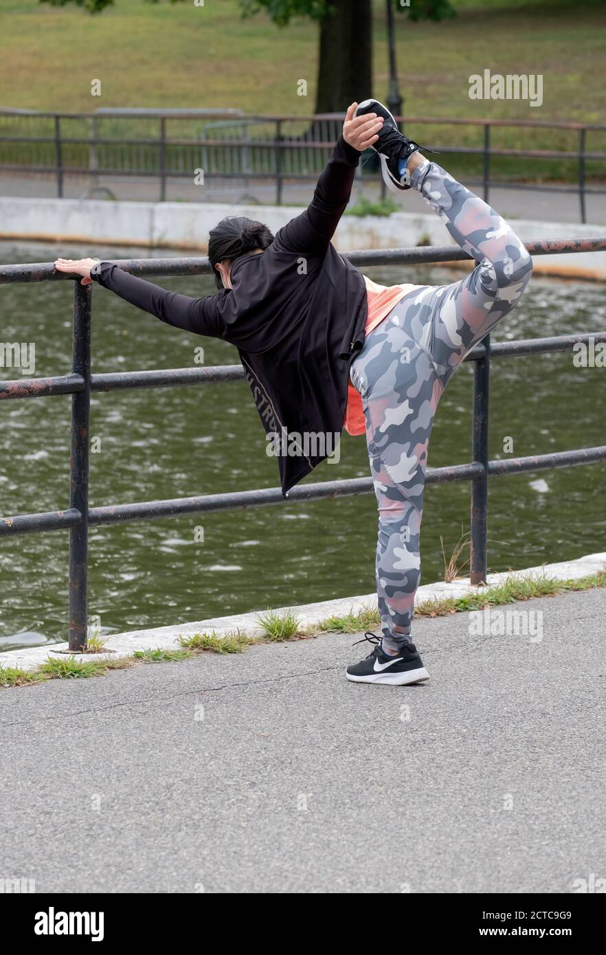 A very limber & nimble Asian American woman stretches before exercising. In a park in Flushing, New York City. Stock Photo