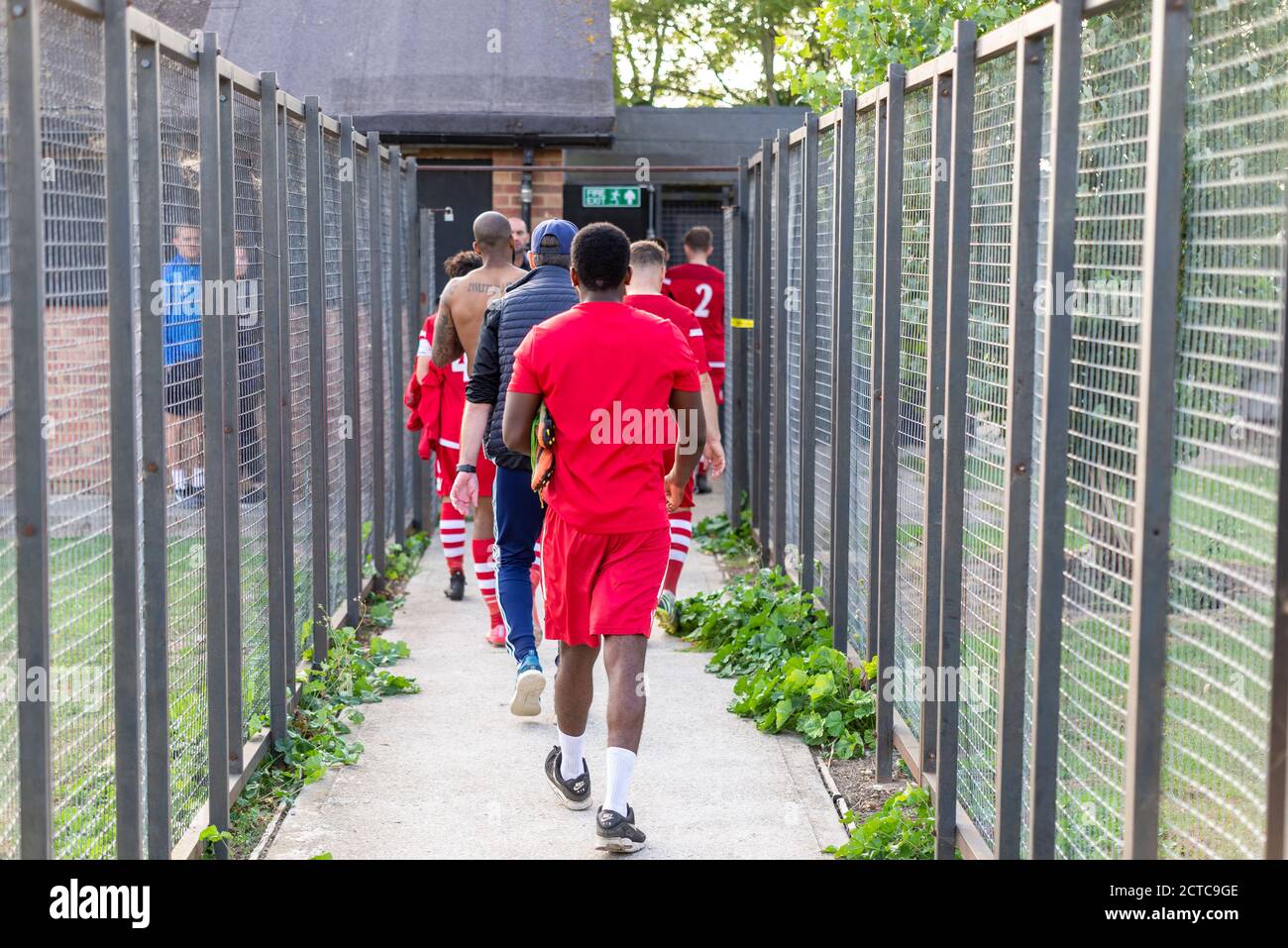 Footballers walking back down a fenced tunnel towards changing rooms after a football match. Cockfosters FC players at Southend Manor ground Stock Photo