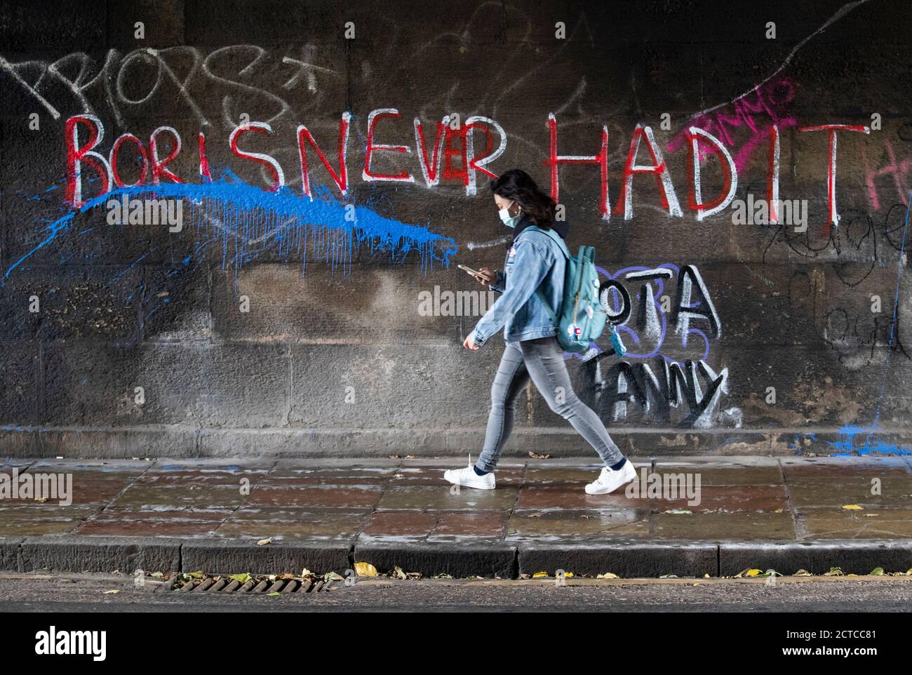 A woman wearing a protective face mask walks past graffiti that reads 'Boris never had it' in Edinburgh city centre, after First Minister Nicola Sturgeon announced a range of new measures to combat the rise in coronavirus cases in Scotland. Stock Photo