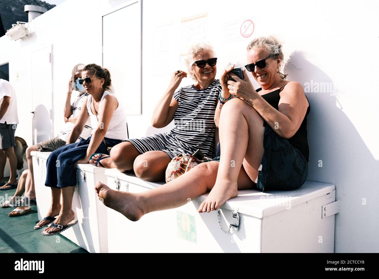 Eldery women siting on a ferry boat in Croatia. They are smiling and typing on ther smartphones. Stock Photo