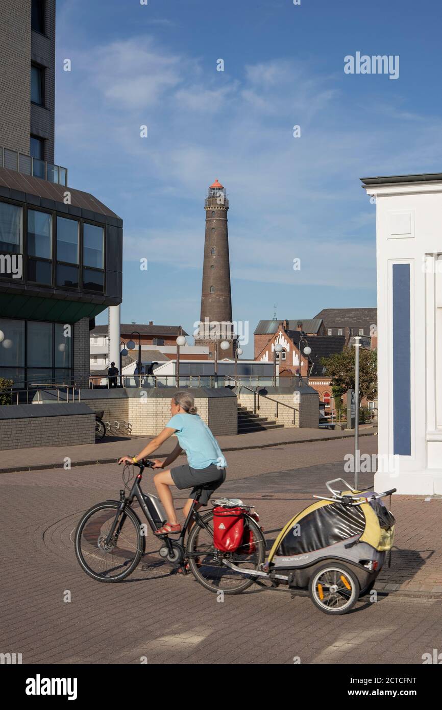 Woman cycling along the promenade with the new lighthouse of Borkum Island in the background, Lower Saxony, Germany, Europe Stock Photo