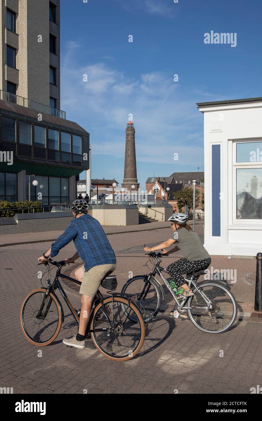 Couple cycling along the promenade with the new lighthouse of Borkum Island in the background, Lower Saxony, Germany, Europe. Stock Photo