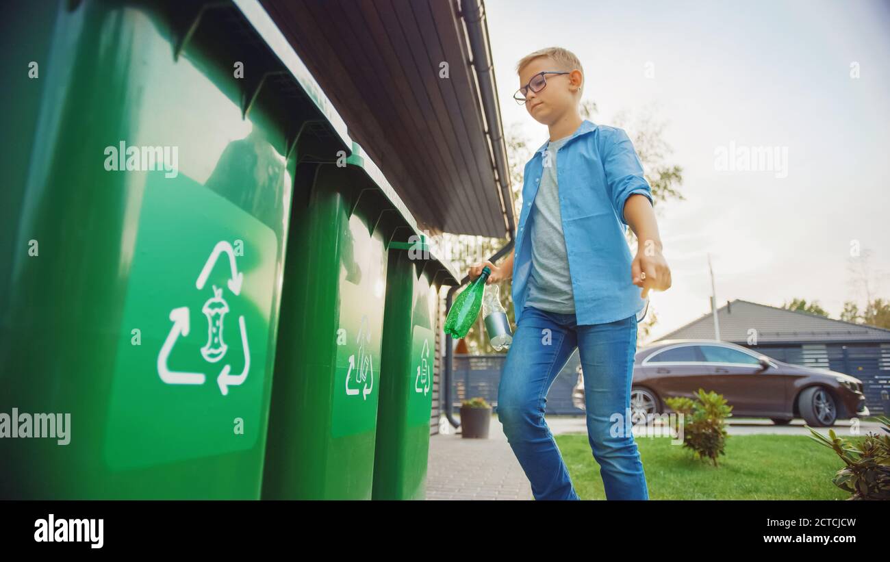 Young Boy is Walking Outside His Home in Order to Throw Away Two Empty Plastic Bottles into a Trash Bin. He Uses Correct Garbage Bin Because This Stock Photo