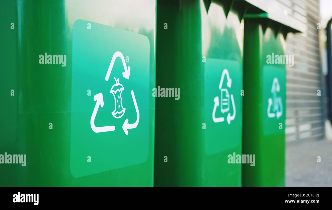 Green colored, plastic garbage bins, with different recycle logos on front, stacked in row against brown wood wall. Concept of waste sorting for food Stock Photo