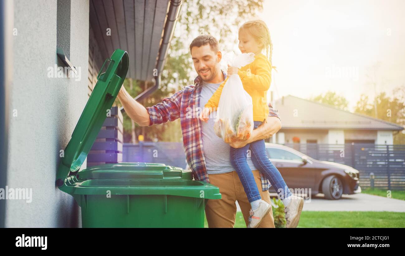 Father Holding a Young Girl and Throwing Away a Food Waste into the Trash. They Use Correct Garbage Bins Because This Family is Sorting Waste and Stock Photo