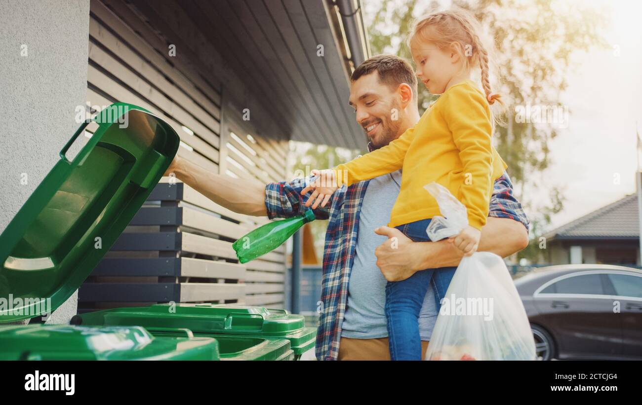 Father Holding a Young Girl and Throw Away an Empty Bottle and Food Waste into the Trash. They Use Correct Garbage Bins Because This Family is Sorting Stock Photo