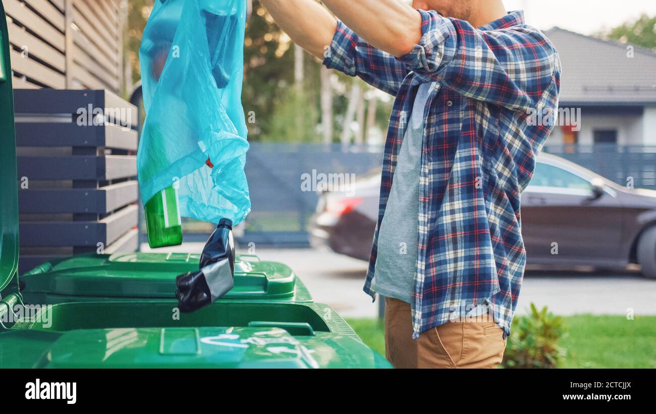 Caucasian Man in Checkered Shirt is Throwing Away Bottles from a Plastic Bag into the Trash Bin. He Uses Correct Garbage Bin Because This Family is Stock Photo