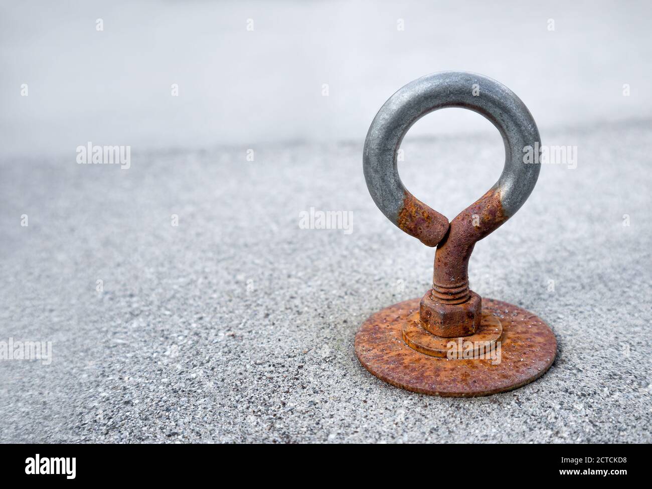 Rusty eye loop or loop screw. Close up. Bolted to an outdoor cement tile covering the patio drain. Eye loops are used to attach ropes or cables. Stock Photo