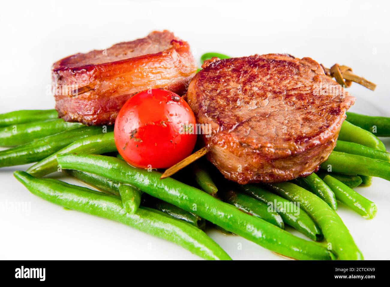 Grilled pork medallions on skewers with string beans and whole tomatoes