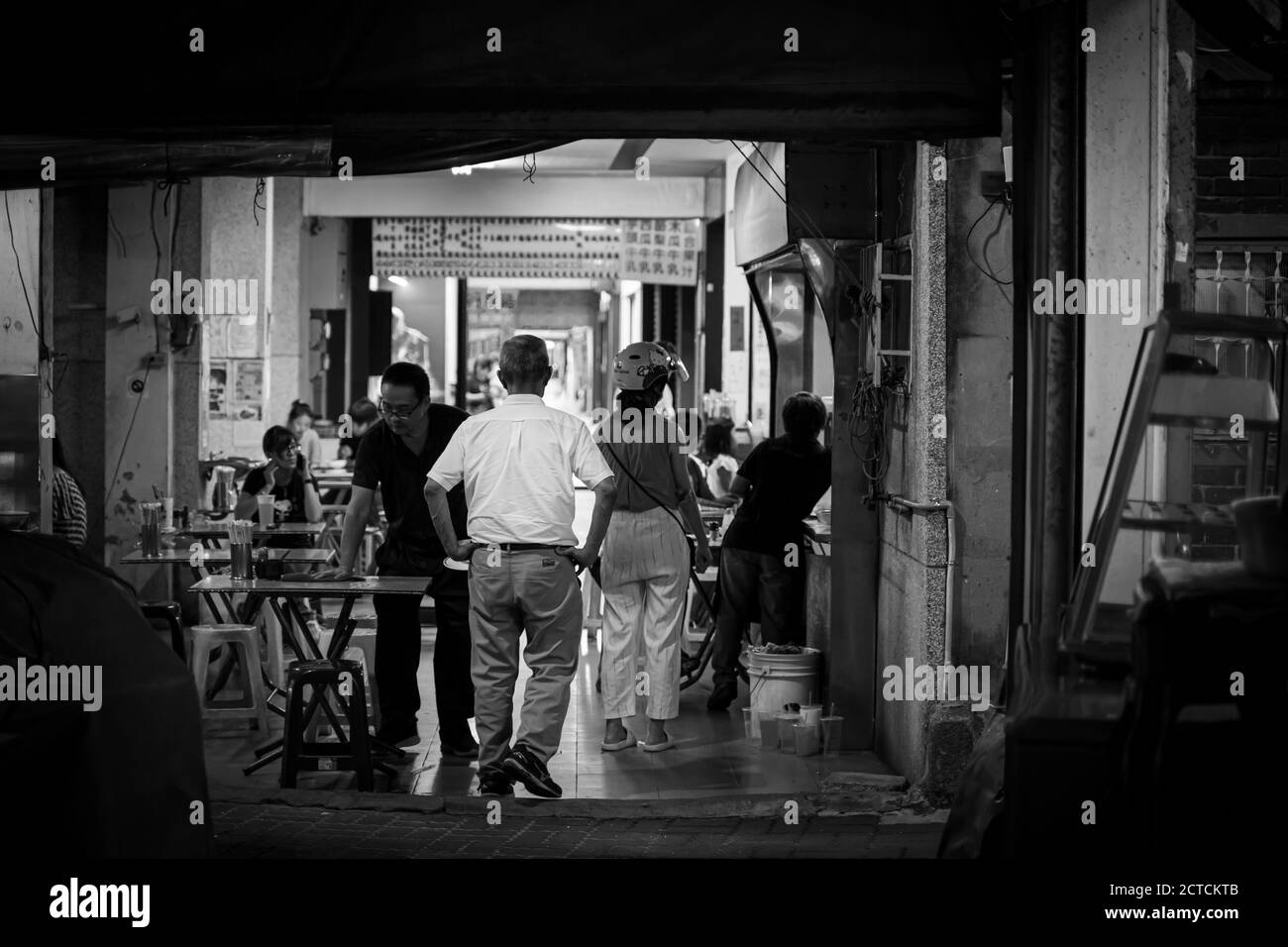 A man with his back walking through a food stand at arcade in Tainan street. Stock Photo
