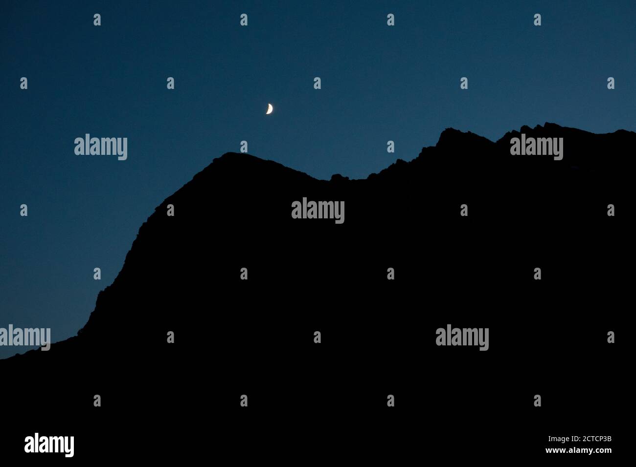 Crescent moon with silhouette of mountain ridge against clear sky at night Stock Photo