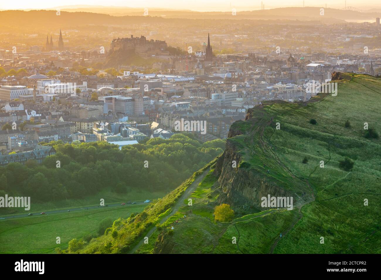 Edinburgh Castle In The Gentle Orange Glow Of A Summer Evening, With Salisbury Crags In The Foreground Stock Photo
