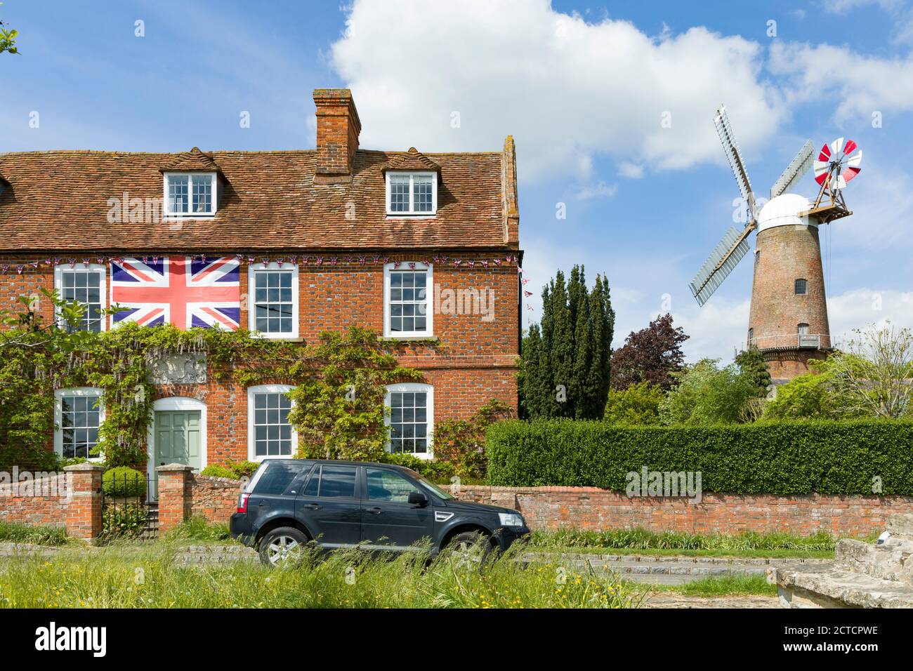 QUAINTON, UK - May 15, 2020. UK village scene in Buckinghamshire, with village green, British flag on a house and working windmill Stock Photo
