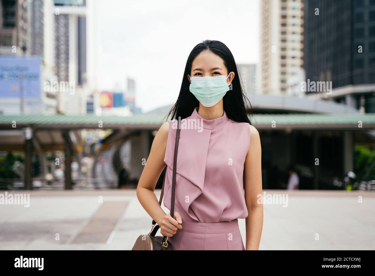 Asian businesswoman wearing protective Covid face covering facing camera, urban setting, city life, pandemic Stock Photo