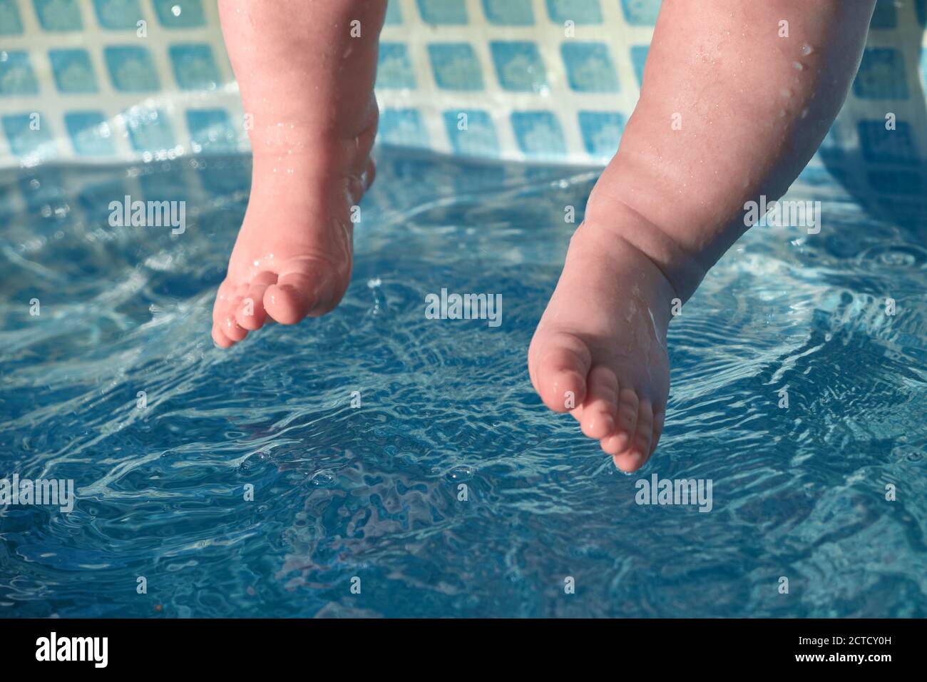 Baby's feet touch the blue water in the pool. Concept of newborn swimming training. Stock Photo