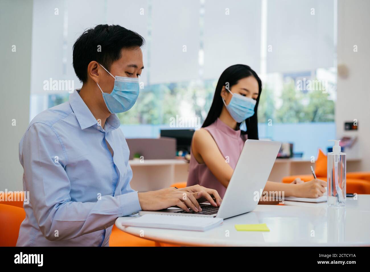 Two business coworkers sitting at table wearing protective Covid face coverings, new normal, protection, health, safety Stock Photo