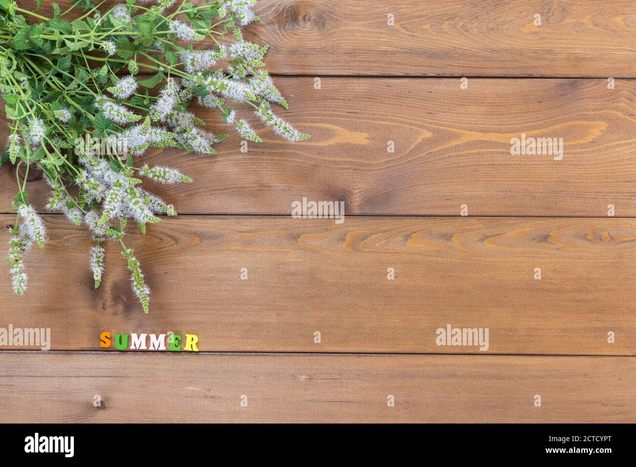 A bouquet of blooming oregano lies on a brown wooden table. Sunny summer. Multicolored letters. Copy space Stock Photo