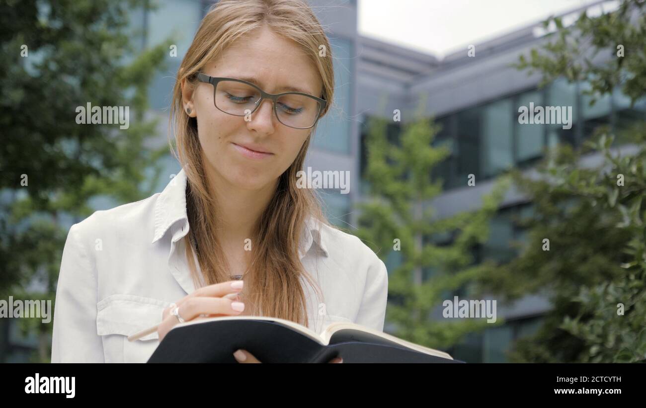 Thoughtful young woman making notes in her note pad and looking Stock Photo