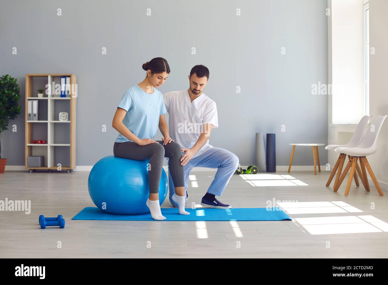 Man doctor chiropractor fixing woman on fitness ball in right position for pain relief Stock Photo