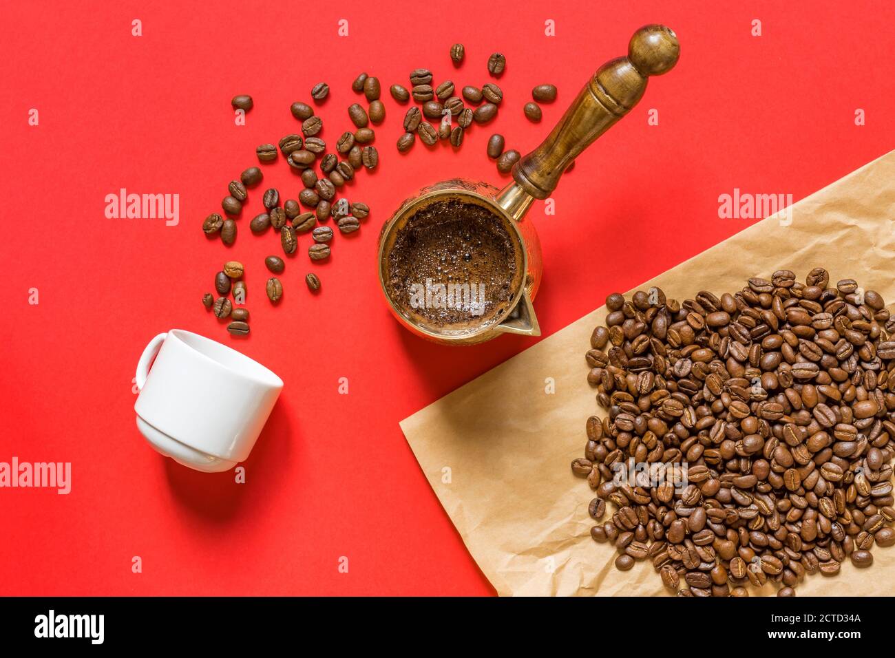 Top view of fresh coffe prepared in  cezve (traditional turkish coffee pot), whte cup and coffee beans on craft paper on red background. Stock Photo
