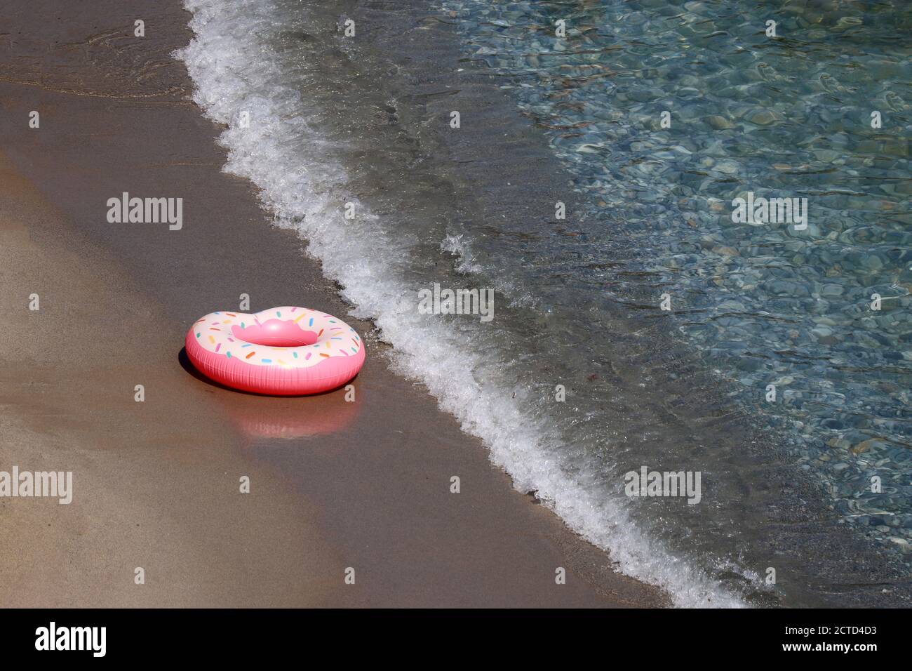 Inflatable ring in donut shape on a sand in sea waves, aerial view. Background for beach vacation, relax and leisure in clean water Stock Photo