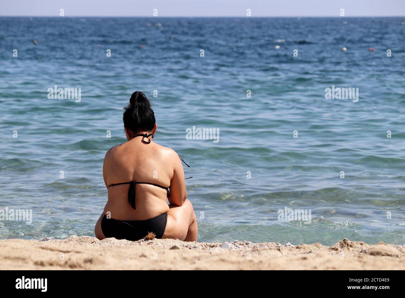 Fat woman sitting on a beach on sea waves background. Overweight and obesity concept Stock Photo