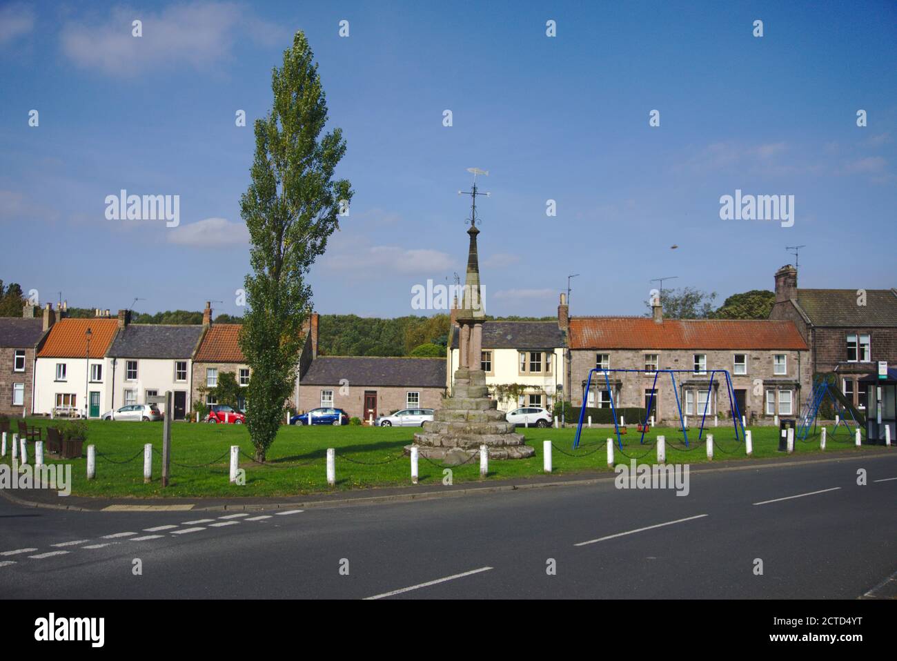 Norham village green, Northumberland, UK, featuring tall tree, monument and children's playground. Stock Photo