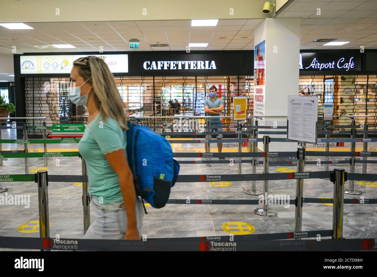 A passanger, a woman wearing a covid protective mask walks with her trolley in the empty Pisa airport, PSA, in Tuscany Italy, before security check. Stock Photo