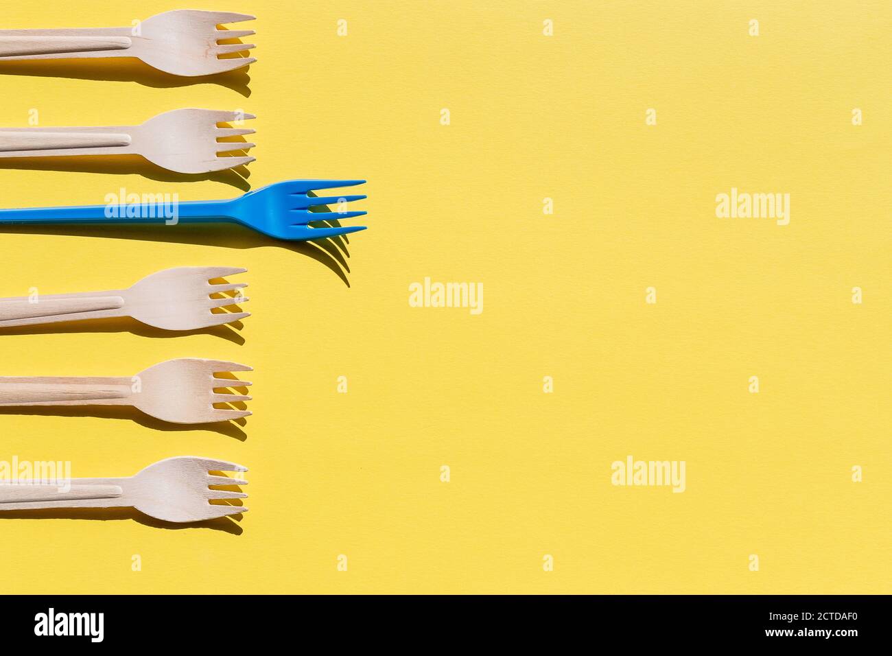 Organic bamboo disposable cutlery vs plastic ones on yellow background