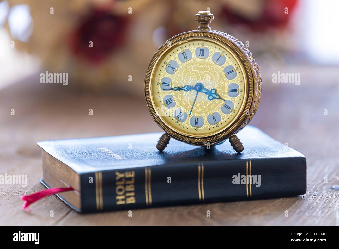 Old alarm clock on Holy bible with flowers on wooden table background Stock Photo