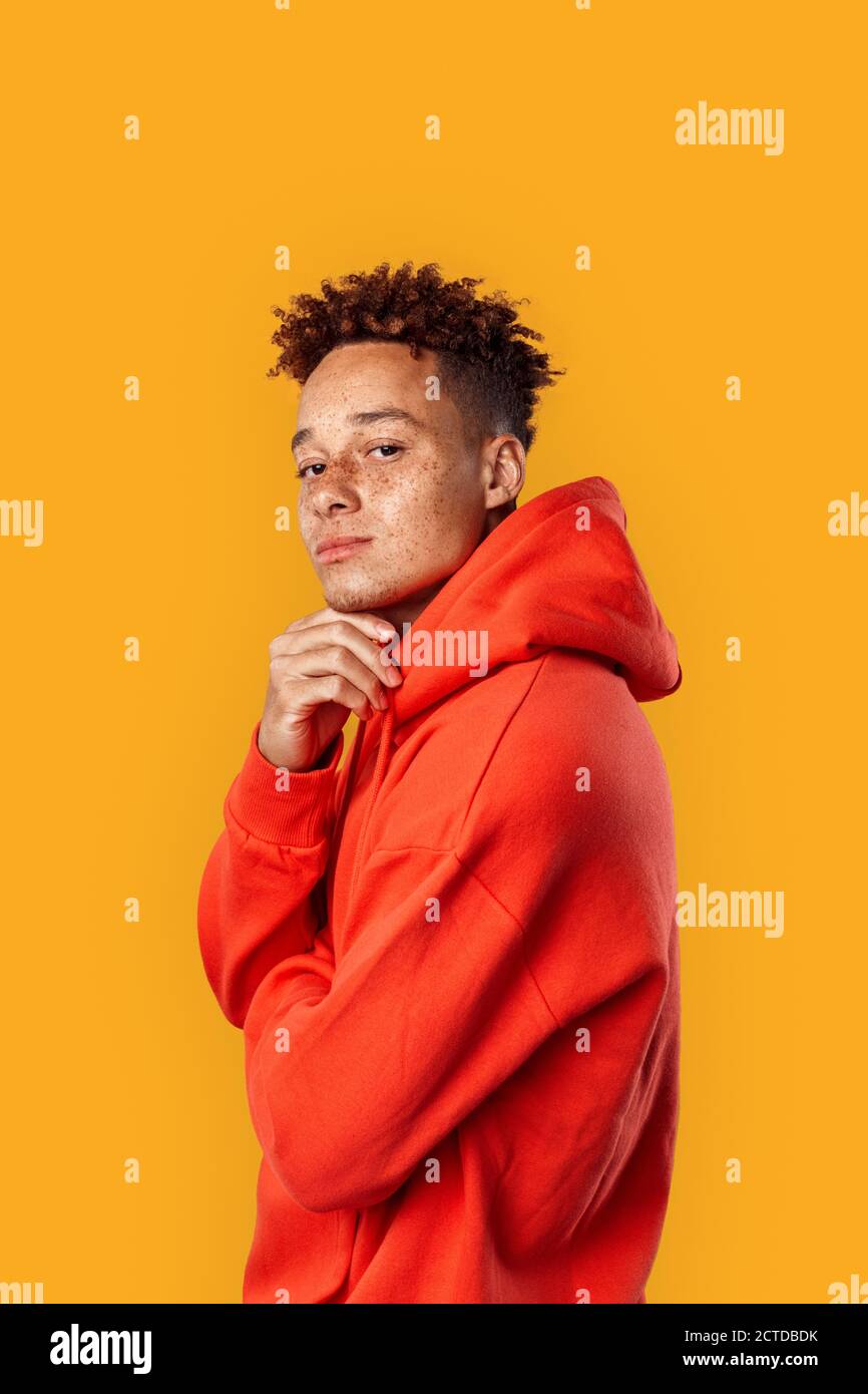 Freestyle Mulatto Freckled Guy In Hoodie Standing Isolated On Yellow Touching Chin Posing To