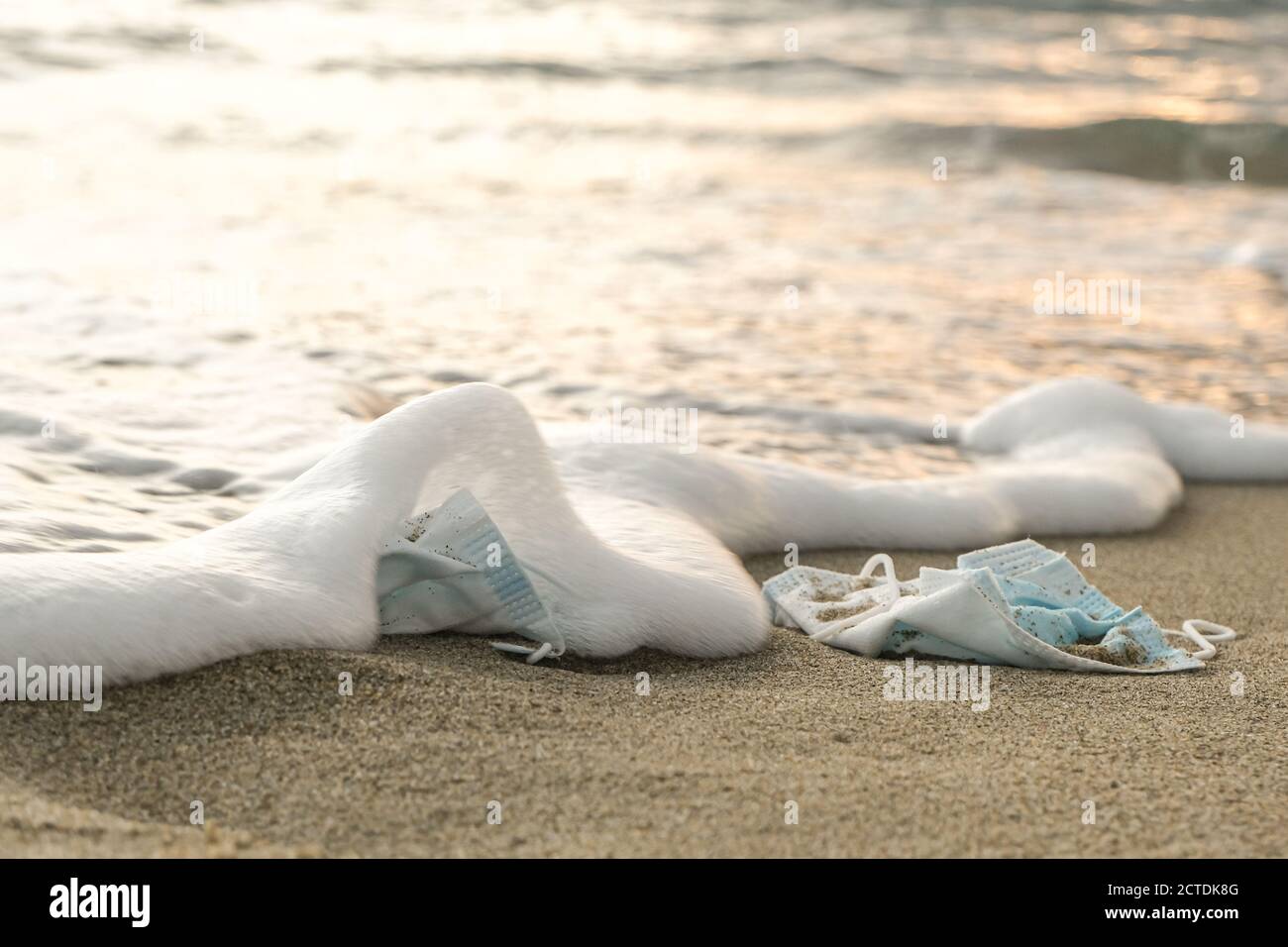 Medical face mask discarded on sea foam on sunset time,covid19 disease pollution Stock Photo