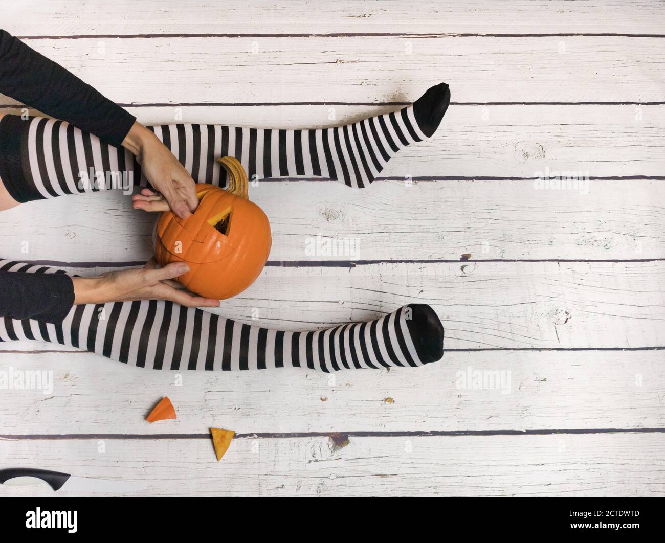 Woman in striped stockings preparing pumpkin for Halloween, on a white wooden background Stock Photo
