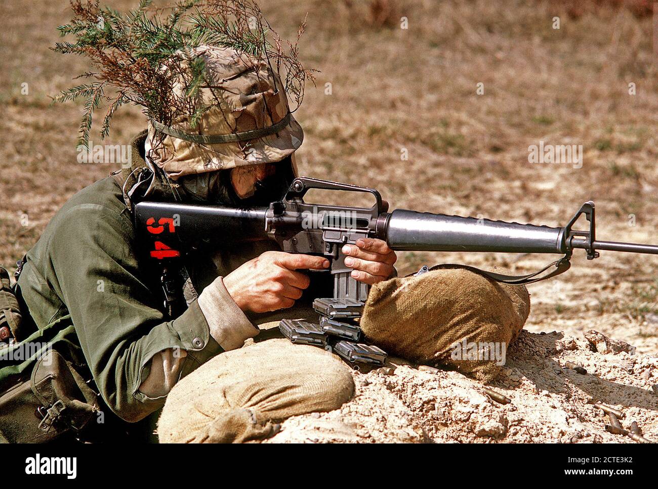 1972 - A U.S. Army soldier fires an M-16A1 rifle during a field exercise.  He is wearing a Nuclear, Biological and Chemical (NBC) protective mask. Stock Photo