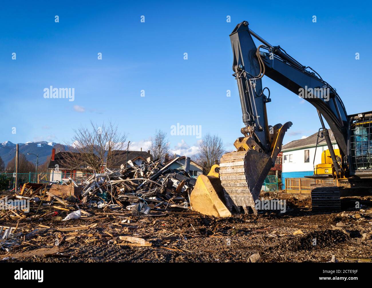 Demolition bulldozer in front of building rubble. Bucket is down, side view. Yellow construction machine with residential buildings and mountains. Stock Photo