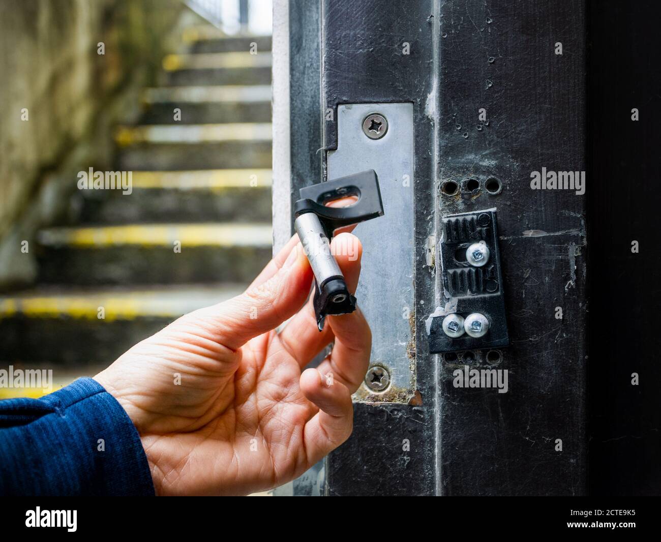 Hand holding broken striking plate from a residential or commercial fire exit door. Damage to door frame and strike plate from thieves / burglars usin Stock Photo