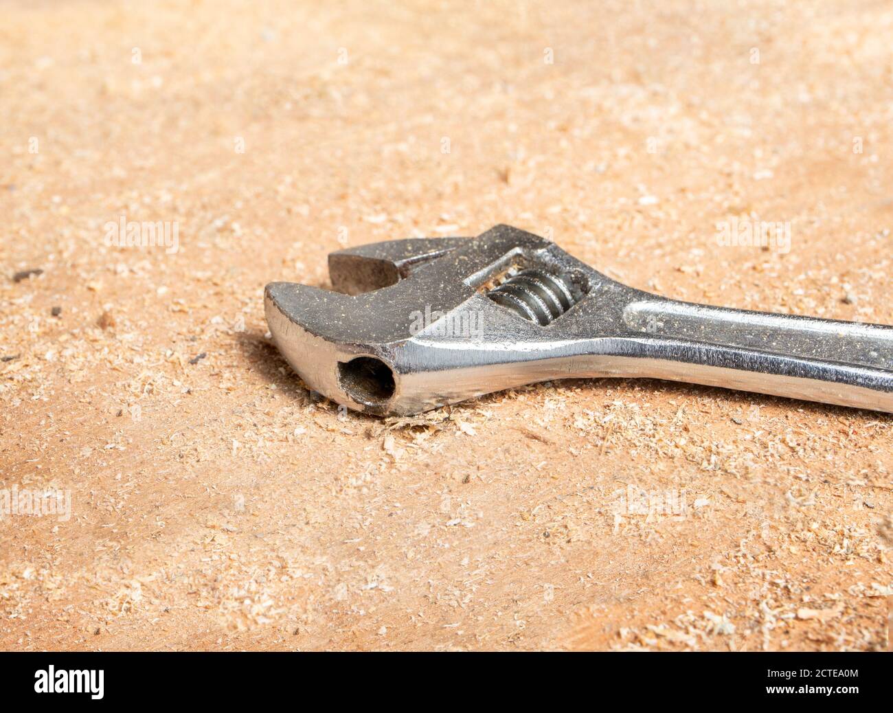 Close up of adjustable wrench in sawdust on work shop table. Perspective view, with focus in center.  Concept for DIY, carpentry or wood workshop. Stock Photo