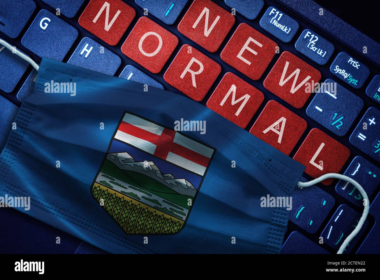 COVID-19 coronavirus new normal concept in the Canadian province of Alberta as shown by Alberta flag on face mask with New Normal on laptop red alert Stock Photo