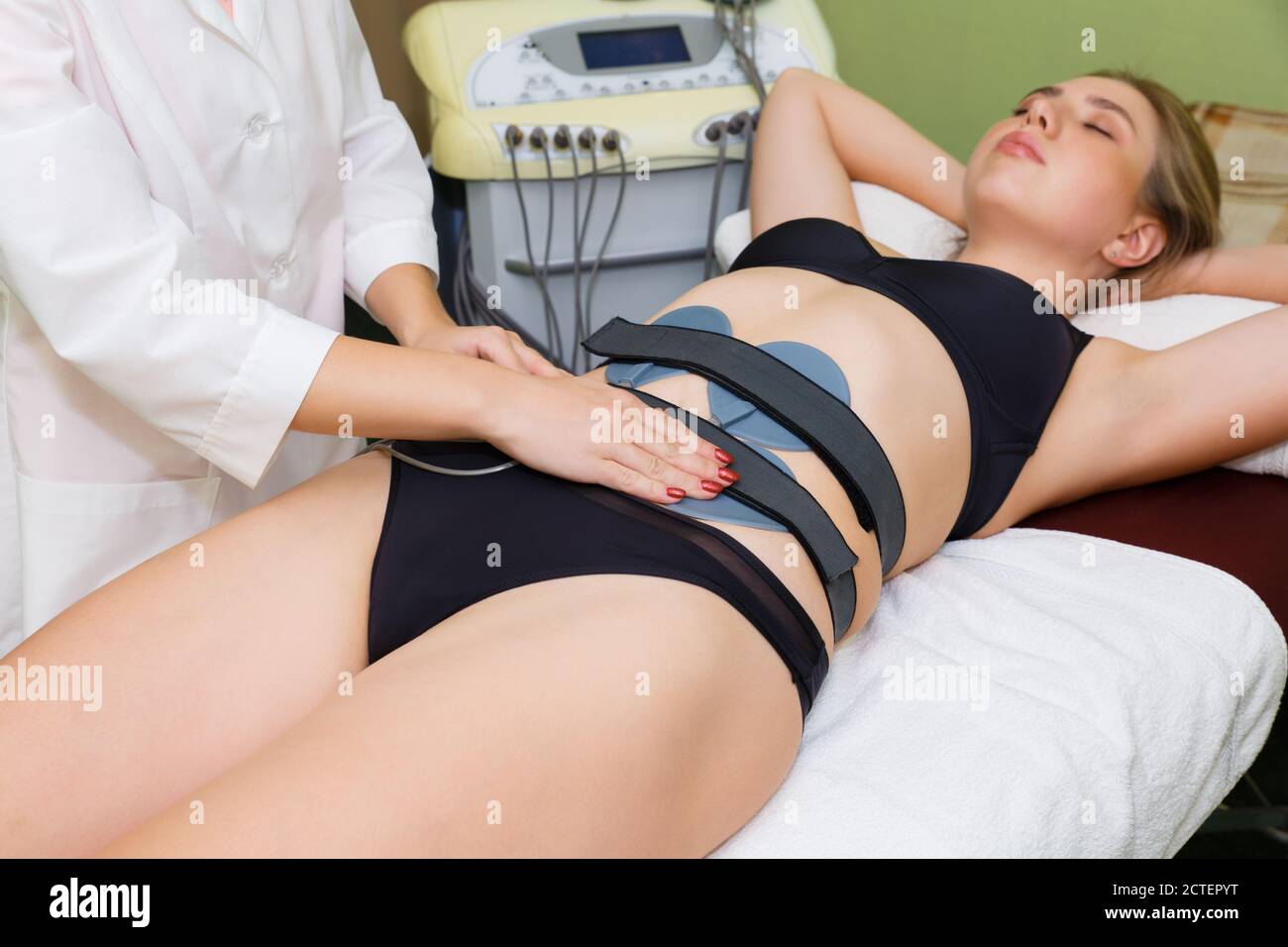 The spa specialist places the muscle myostimulation electrodes on the woman's abdomen. Stock Photo