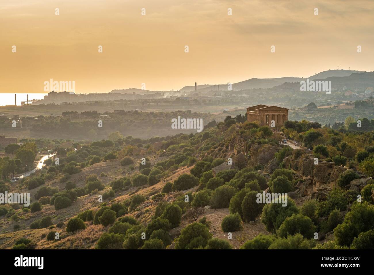 Valley of Temples: Temple of Concord against the industrial landscape on background at sunset. Agrigento, Sicily, Italy. Stock Photo