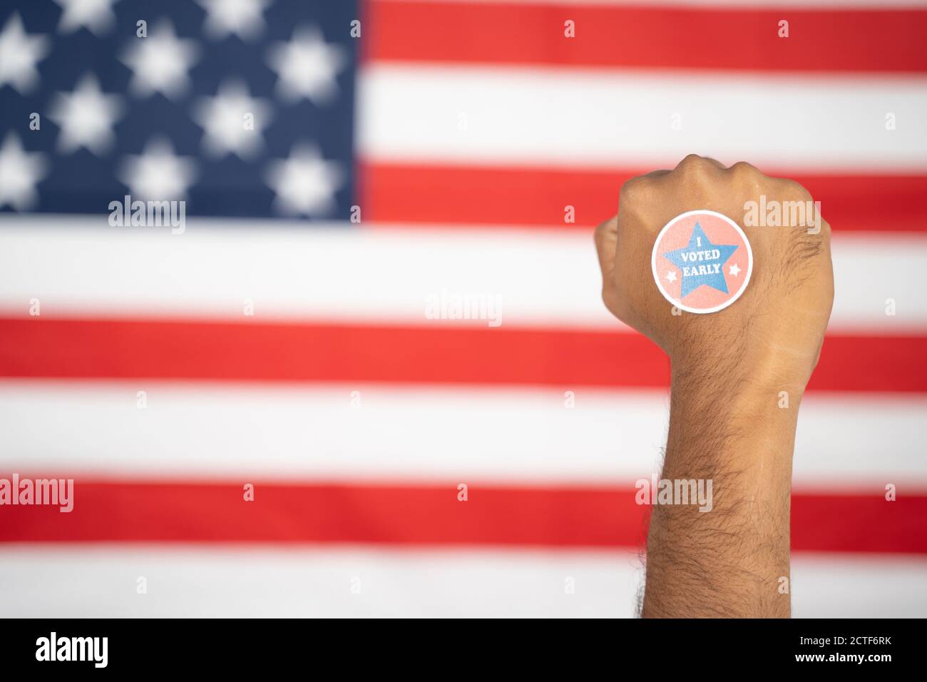 Rising fist with I voted early sticker on hand with US flag as background - Concept of early voting at US election. Stock Photo