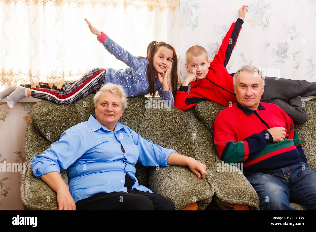 Grandchildren jumping on couch with their grandparents in the living room Stock Photo