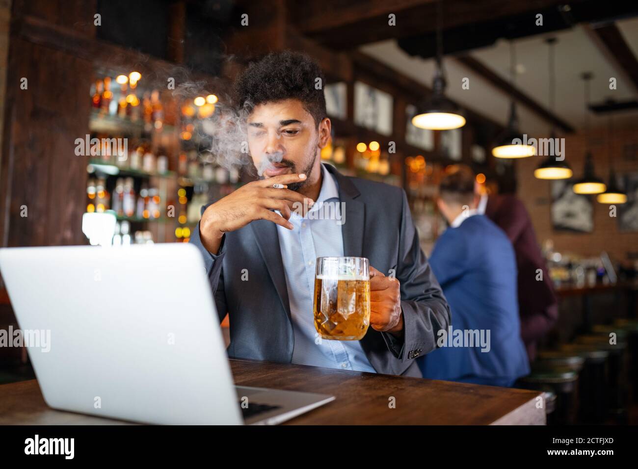 Man drinking beer and smoking cigarette while working on computer. Bad habit concept. Stock Photo