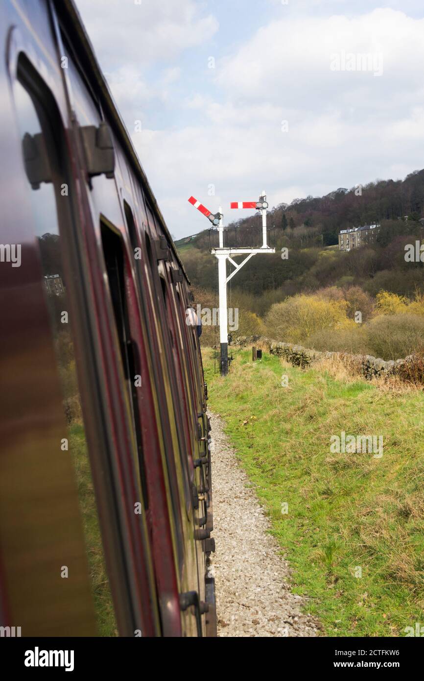 Steam train approaching a junction home signal. The left hand semaphore signal set at clear to permit the train to advance on to a double line section Stock Photo