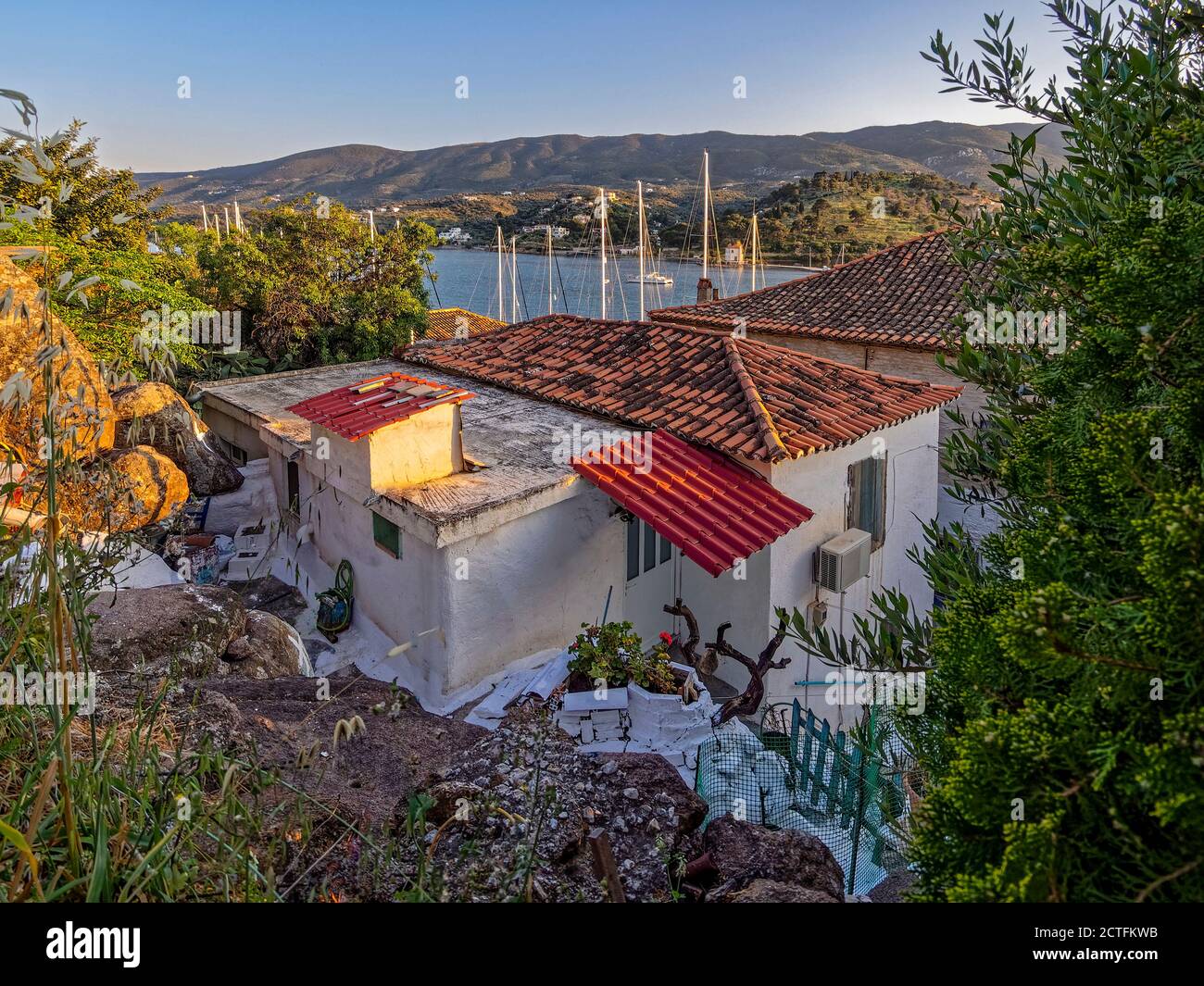House with a View.The masts of the yachts and the blue sea on the horizon testify about Poros port hidden behind the old houses perched on the rocks a Stock Photo